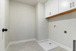 Clothes washing area with hookup for a washing machine, hookup for an electric dryer, cabinets, and light tile patterned flooring