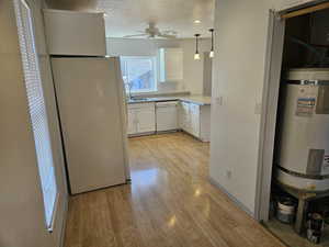 Kitchen featuring white appliances, light hardwood / wood-style flooring, a textured ceiling, white cabinets, and strapped water heater