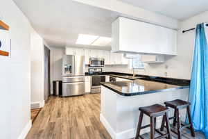 Kitchen with white cabinetry, stainless steel appliances, sink, kitchen peninsula, and light wood-type flooring