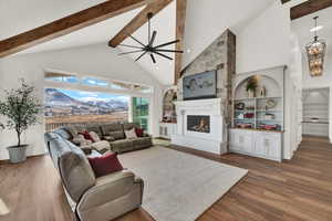 Living room with ceiling fan with notable chandelier, a towering ceiling, a fireplace, built in features, and hardwood / wood-style flooring