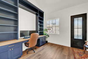 Home office with built in shelves, built in desk, and light hardwood / wood-style floors