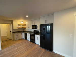 Kitchen featuring sink, black appliances, white cabinetry, and light hardwood / wood-style flooring