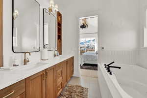 Bathroom featuring tiled tub, tile patterned flooring, vaulted ceiling, and vanity