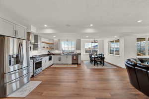 Kitchen featuring hardwood / wood-style floors, pendant lighting, wall chimney range hood, and stainless steel appliances