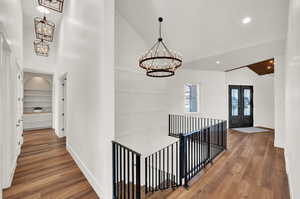 Hall featuring french doors, hardwood / wood-style flooring, built in shelves, high vaulted ceiling, and a chandelier