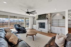 Living room featuring a textured ceiling, a stone fireplace, built in features, light wood-type flooring, and a mountain view