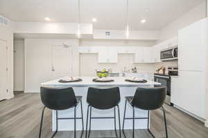 Kitchen with pendant lighting, white cabinets, a center island, stainless steel appliances, and light hardwood / wood-style flooring