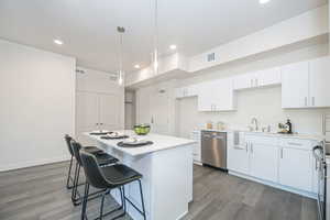 Kitchen with stainless steel dishwasher, dark hardwood / wood-style flooring, decorative light fixtures, white cabinets, and a center island