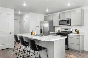 Kitchen with sink, stainless steel appliances, a center island with sink, and light hardwood / wood-style floors