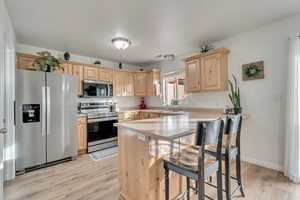 Kitchen featuring light brown cabinetry, appliances with stainless steel finishes, a kitchen breakfast bar, light hardwood / wood-style flooring, and kitchen peninsula