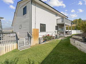 Back of property featuring a balcony, central air condition unit, and a yard