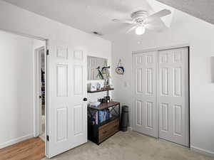 Bedroom featuring ceiling fan, light colored carpet, a textured ceiling, and a closet