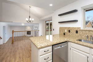 Kitchen with stainless steel dishwasher, white cabinets, sink, backsplash, and lofted ceiling