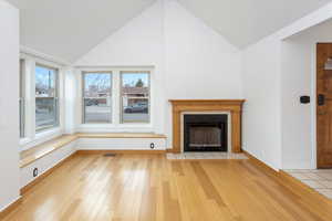 Unfurnished living room featuring a tile fireplace, light hardwood / wood-style flooring, and vaulted ceiling