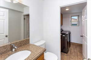 Bathroom featuring vanity, washing machine and clothes dryer, toilet, and hardwood / wood-style flooring