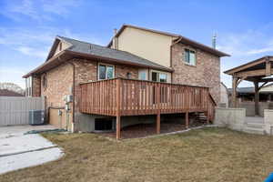 Rear view of property with cooling unit, a wooden deck, and a yard