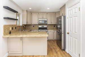 Kitchen with appliances with stainless steel finishes, tasteful backsplash, light hardwood / wood-style floors, sink, and kitchen peninsula