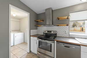 Kitchen featuring decorative backsplash, white cabinets, stainless steel appliances, wall chimney exhaust hood, and light tile patterned flooring