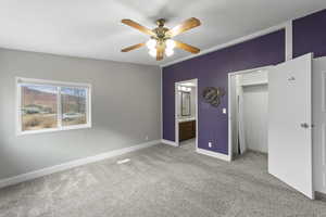 Unfurnished bedroom featuring crown molding, ensuite bathroom, ceiling fan, light colored carpet, and a closet