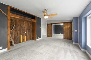 Unfurnished bedroom featuring ceiling fan, lofted ceiling, a barn door, and carpet flooring