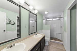 Bathroom featuring a textured ceiling, tile patterned flooring, vanity, toilet, and a tile shower