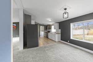 Kitchen featuring wall chimney range hood, stainless steel appliances, white cabinetry, and a healthy amount of sunlight