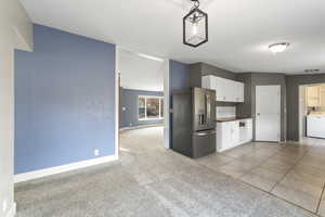 Kitchen with washer / clothes dryer, hanging light fixtures, light carpet, stainless steel refrigerator with ice dispenser, and white cabinets