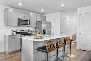 Kitchen with light hardwood / wood-style floors, appliances with stainless steel finishes, sink, a center island with sink, and gray cabinets