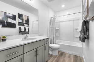 Full bathroom with vanity, hardwood / wood-style flooring, shower / bath combo with shower curtain, and toilet