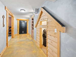 Corridor featuring wooden walls, built in features, a textured ceiling, and concrete flooring