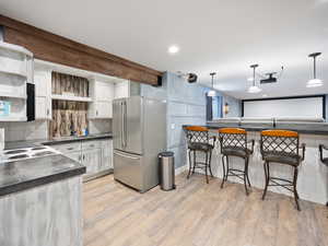 Kitchen featuring stainless steel fridge, hanging light fixtures, light wood-type flooring, white cabinetry, and stove