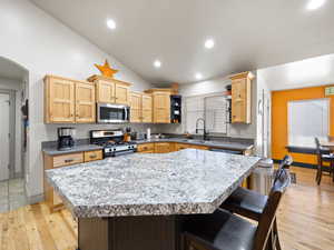 Kitchen with appliances with stainless steel finishes, lofted ceiling, light brown cabinets, sink, and light hardwood / wood-style flooring