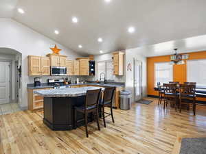 Kitchen with vaulted ceiling, decorative light fixtures, light wood-type flooring, a kitchen island, and stainless steel appliances