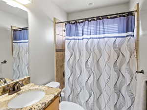 Bathroom featuring a shower with curtain, toilet, and vanity