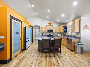 Kitchen with sink, a kitchen bar, a kitchen island, lofted ceiling, and stainless steel appliances