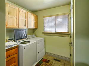 Clothes washing area with washing machine and clothes dryer, light tile patterned floors, and cabinets