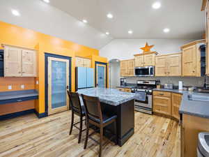 Kitchen featuring light brown cabinets, appliances with stainless steel finishes, light wood-type flooring, a center island, and lofted ceiling