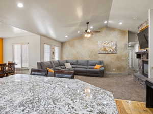 Living room with ceiling fan with notable chandelier, a stone fireplace, light hardwood / wood-style floors, and lofted ceiling