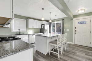 Kitchen featuring appliances with stainless steel finishes, a center island, white cabinetry, sink, and hanging light fixtures