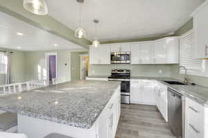 Kitchen with appliances with stainless steel finishes, a kitchen island, a kitchen bar, white cabinetry, and sink