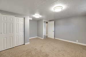 Unfurnished bedroom featuring light colored carpet, a textured ceiling, and a closet