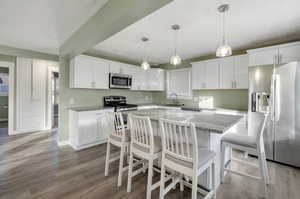 Kitchen with pendant lighting, white cabinets, a center island, stainless steel appliances, and light stone counters