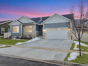 View of front of house featuring an attached garage, stone siding, driveway, a lawn, and board and batten siding