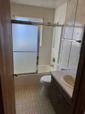 Full bathroom featuring a textured ceiling, combined bath / shower with glass door, vanity, and toilet
