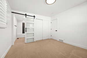 Unfurnished bedroom featuring a closet, a barn door, and light carpet