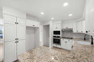 Kitchen featuring white cabinets, tasteful backsplash, sink, oven, and light stone counters