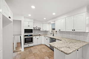 Kitchen with light stone countertops, white cabinetry, stainless steel appliances, decorative backsplash, and sink