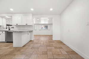 Kitchen featuring tasteful backsplash, white cabinetry, stainless steel dishwasher, sink, and light stone counters