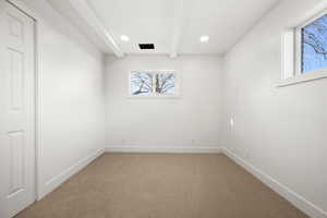 Spare room featuring beamed ceiling and light colored carpet