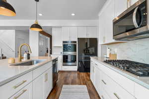 Kitchen with pendant lighting, white cabinetry, stainless steel appliances, sink, and light stone counters